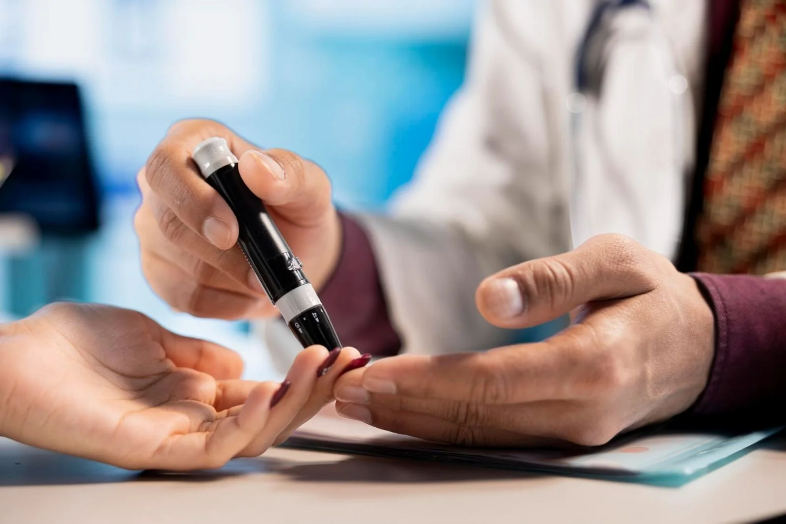 Close-up of a person's finger with a blood droplet near a glucometer on a wooden surface.